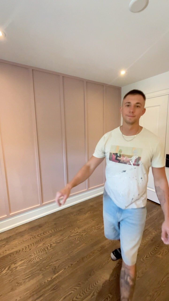 Man standing in a room with a pink accent wall featuring decorative picture frame trim.