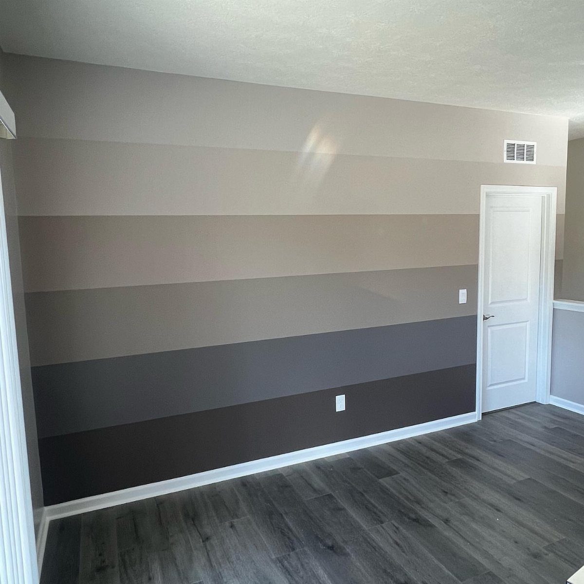 A room with a grey striped accent wall and grey wood laminate flooring.