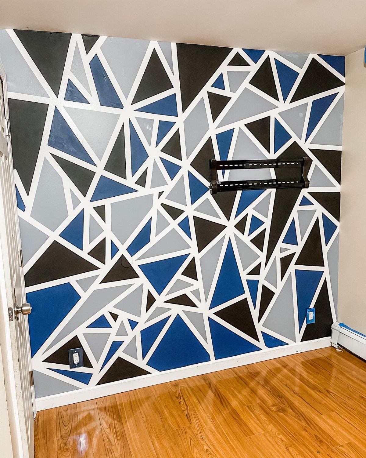 Geometric painted accent wall with blue, grey, black, and white triangular shapes and a black shelf.
