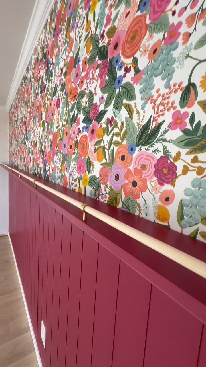 Floral patterned wallpaper above dark pink wainscoting in a room with a wooden chair rail.
