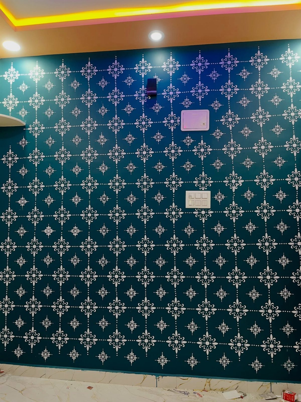 Teal wall decorated with a repeating white ornate stencil pattern and electrical fixtures.