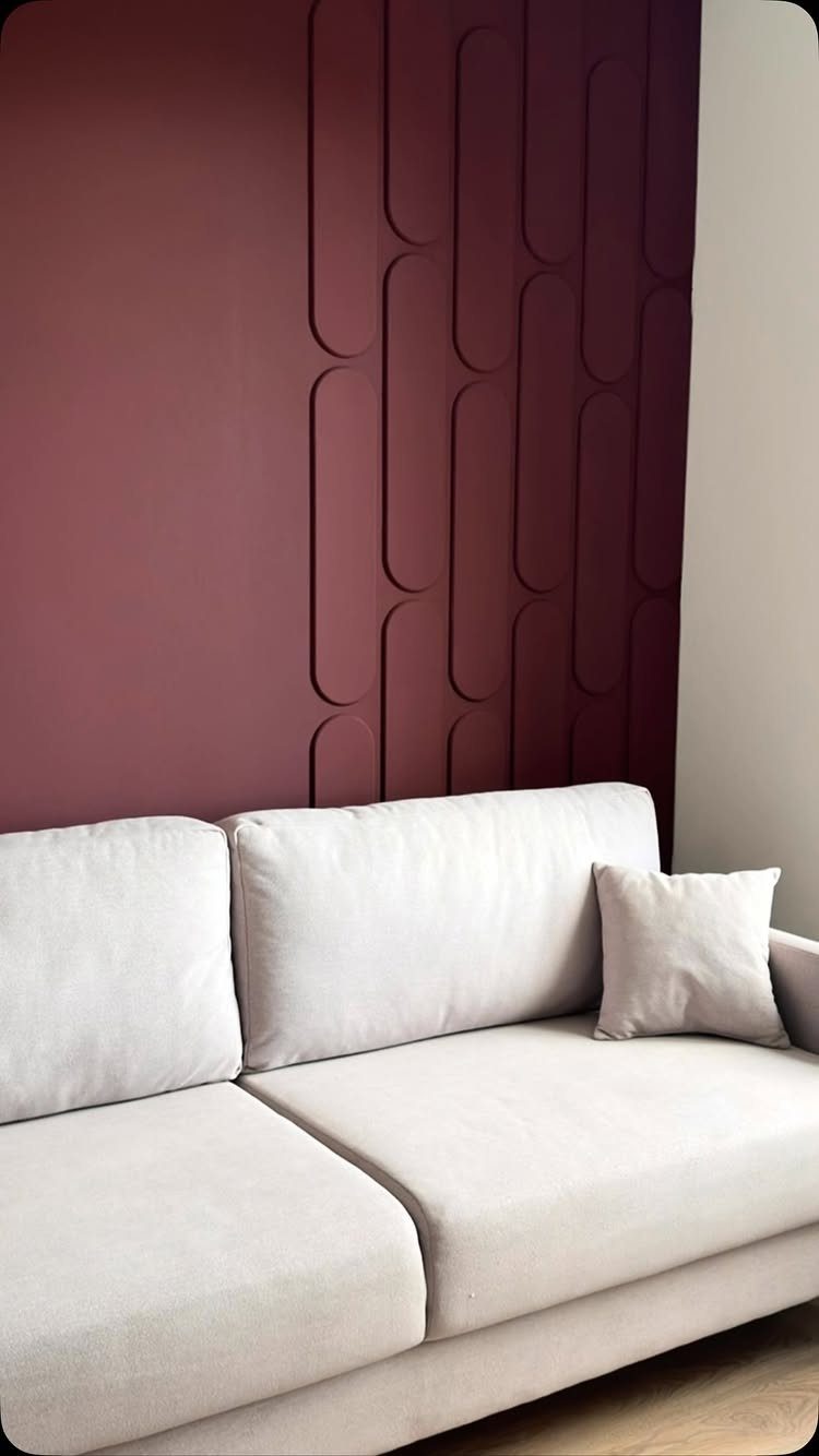 Burgundy accent wall with raised geometric pill shapes behind a light grey sofa.