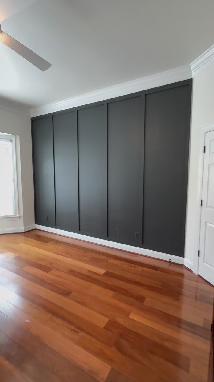 Dark grey board and batten accent wall installed in a room with hardwood floors.