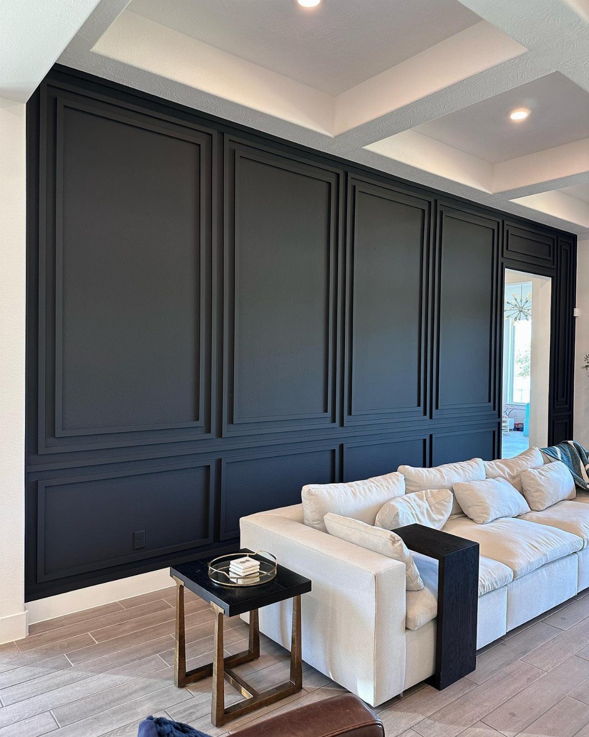 Black wall with decorative picture frame molding behind a white sectional sofa and side table.
