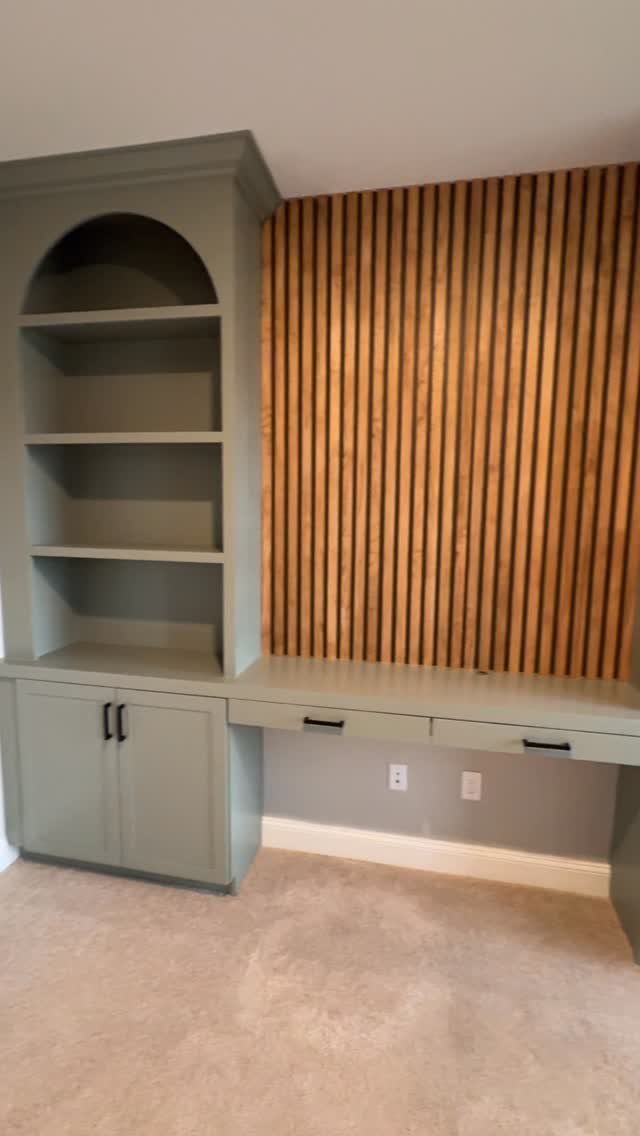 Sage green built-in shelving unit with an arched top next to a vertical wood slat wall.