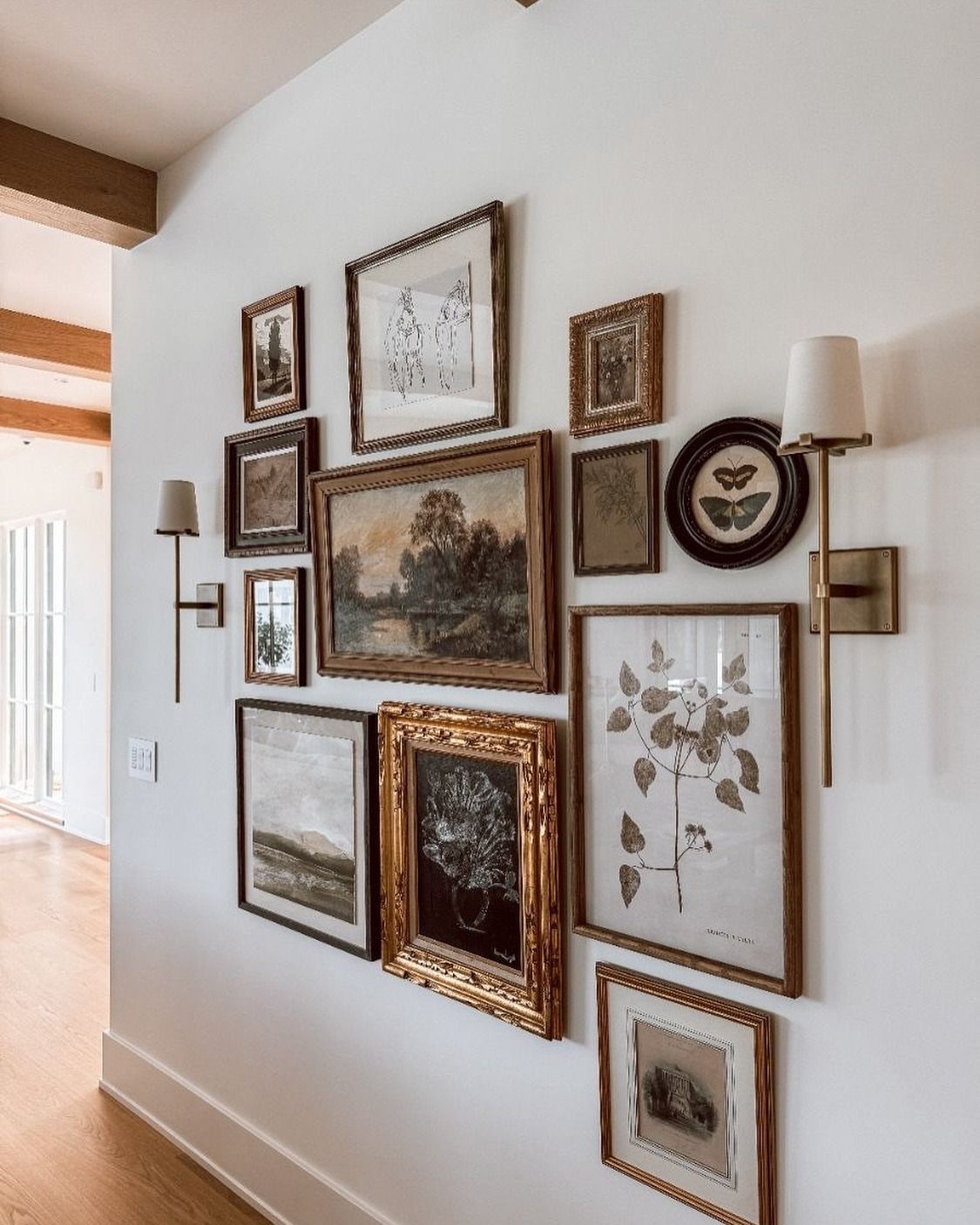 Framed artworks of various sizes and styles arranged in a gallery wall on a white wall.