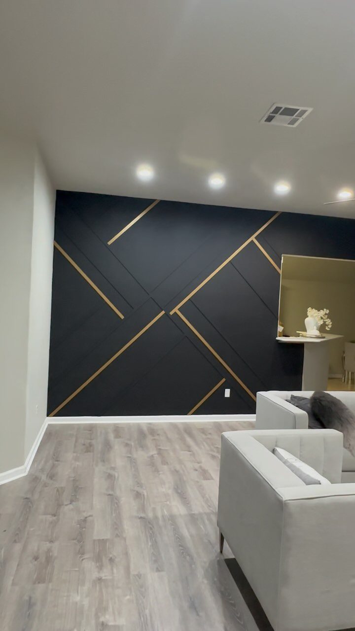 Dark charcoal accent wall with gold geometric lines in a modern living room setting.