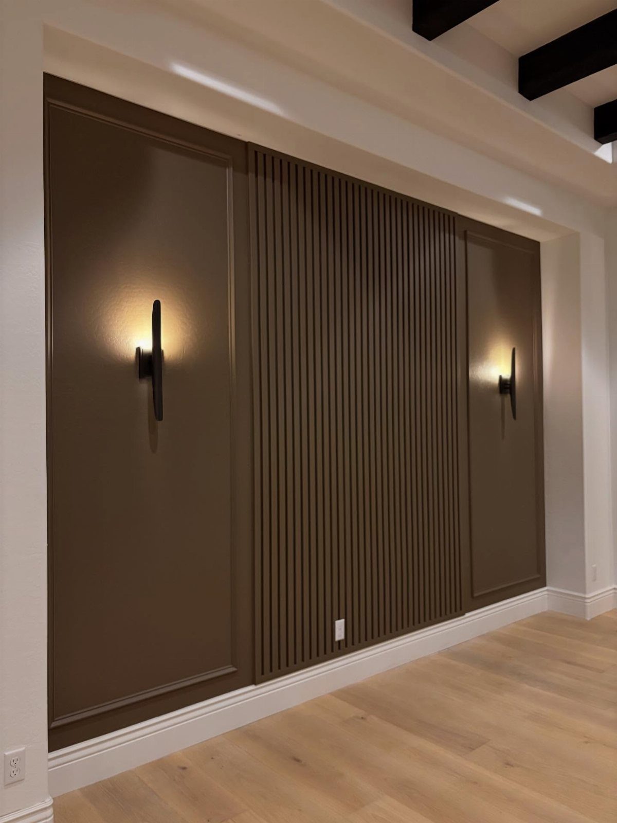 Brown accent wall with central vertical wood slats and side panels featuring decorative molding and sconces.