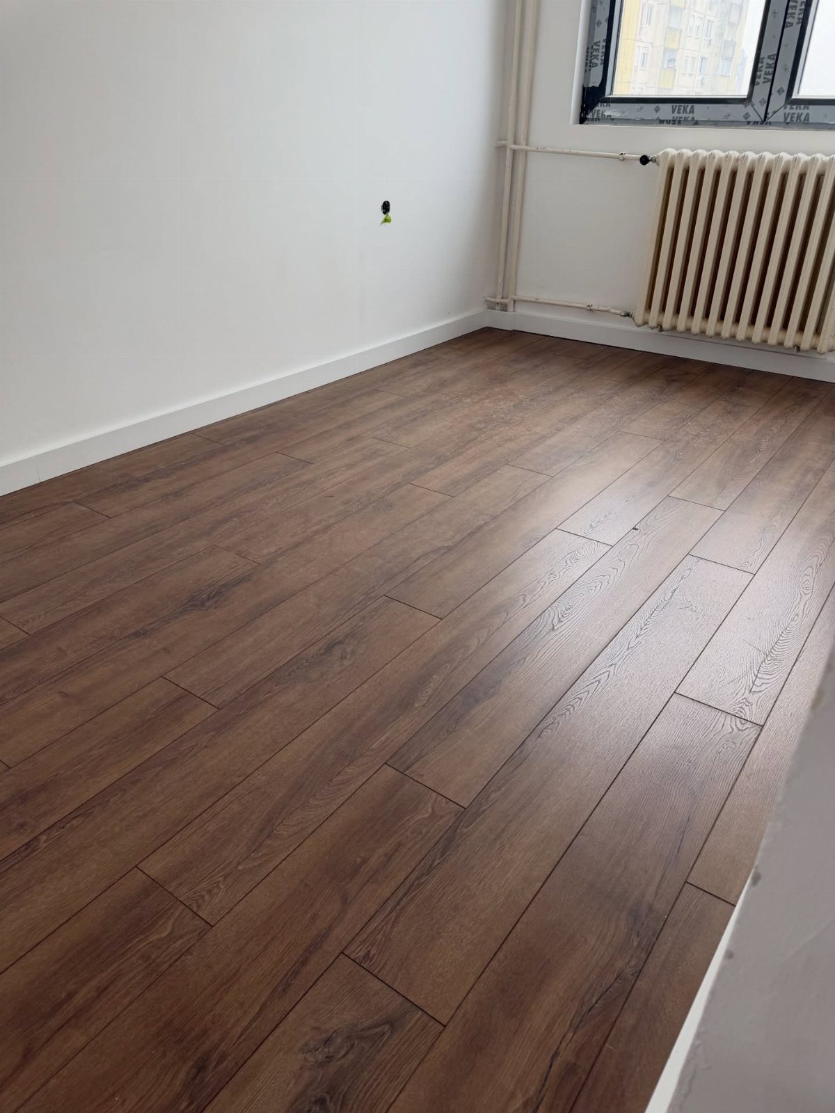 10 Affordable Flooring Ideas for Every Room in 2026 2 Dark brown wood-look flooring planks installed in an empty room with white walls.