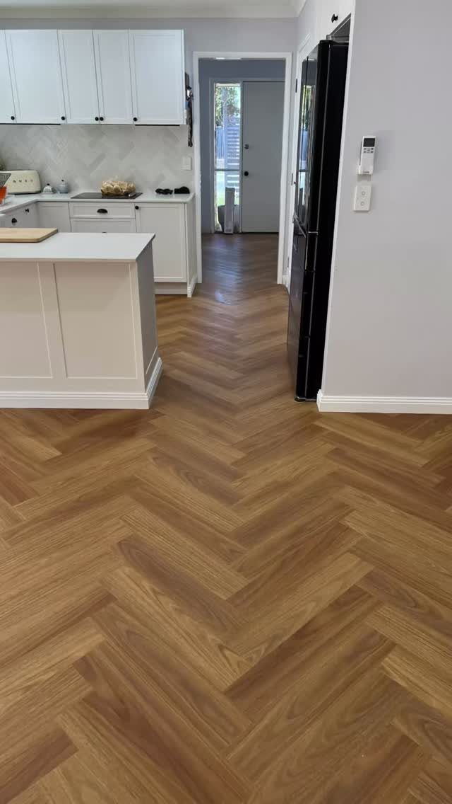 10 Affordable Flooring Ideas for Every Room in 2026 1 Light brown herringbone pattern laminate flooring in a modern white kitchen and hallway.