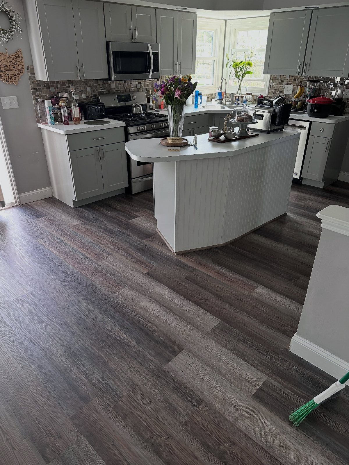 10 Affordable Flooring Ideas for Every Room in 2026 6 Grey wood-look planks covering the floor of a modern kitchen with grey cabinets.