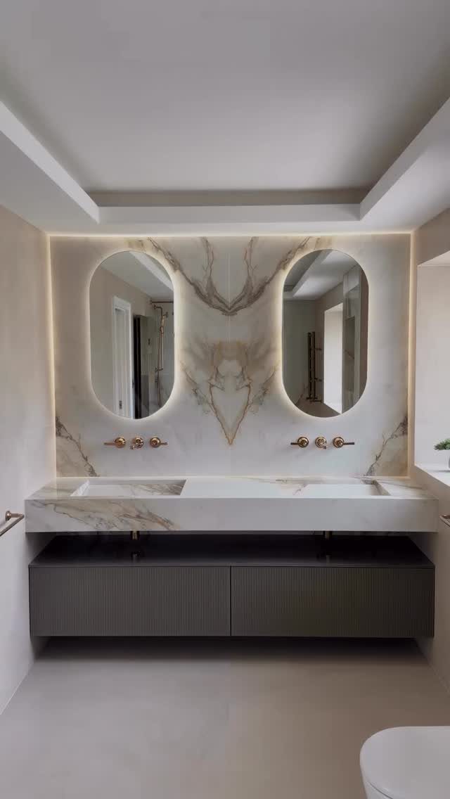 Marble backsplash with gold veining and two oval backlit mirrors above a white vanity.