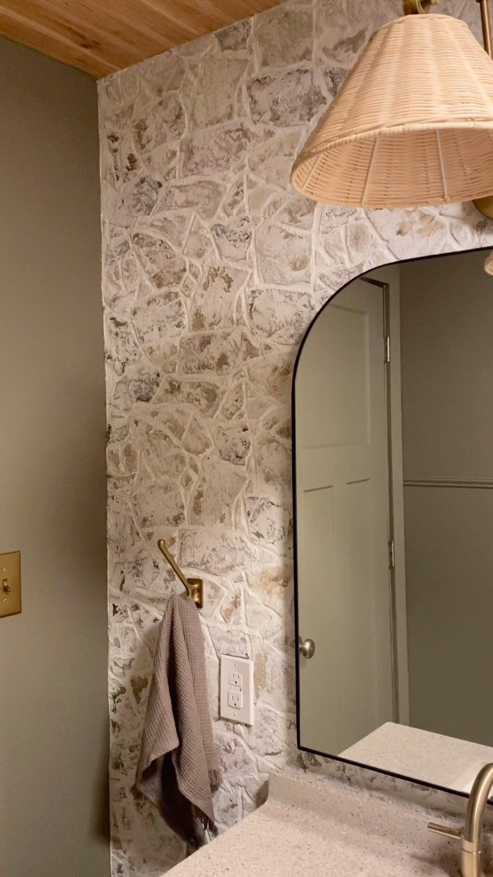 Natural stone tiles covering a bathroom wall next to a vanity mirror and countertop.
