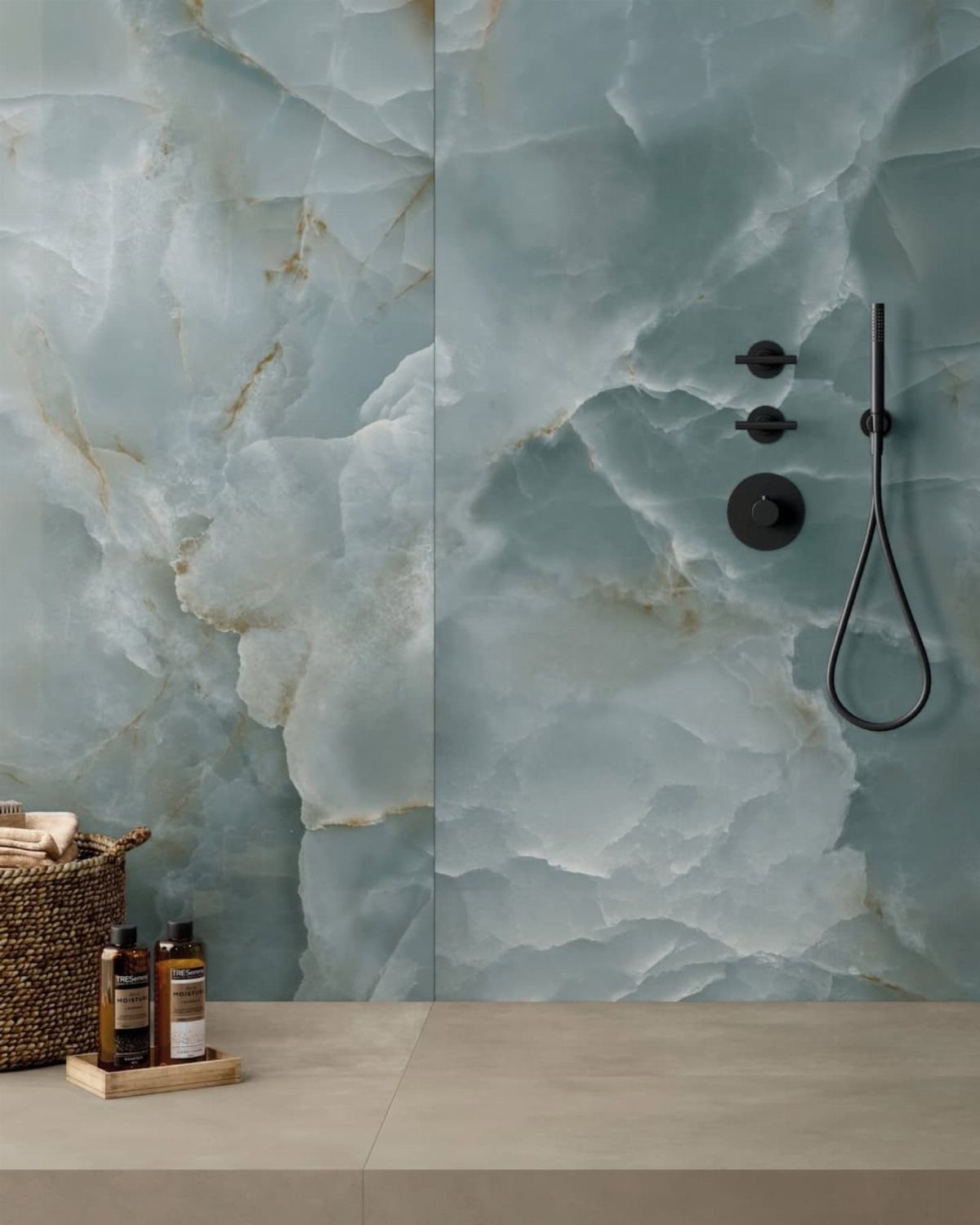 Blue and teal onyx tiles with gold veining installed on a bathroom wall with black fixtures.