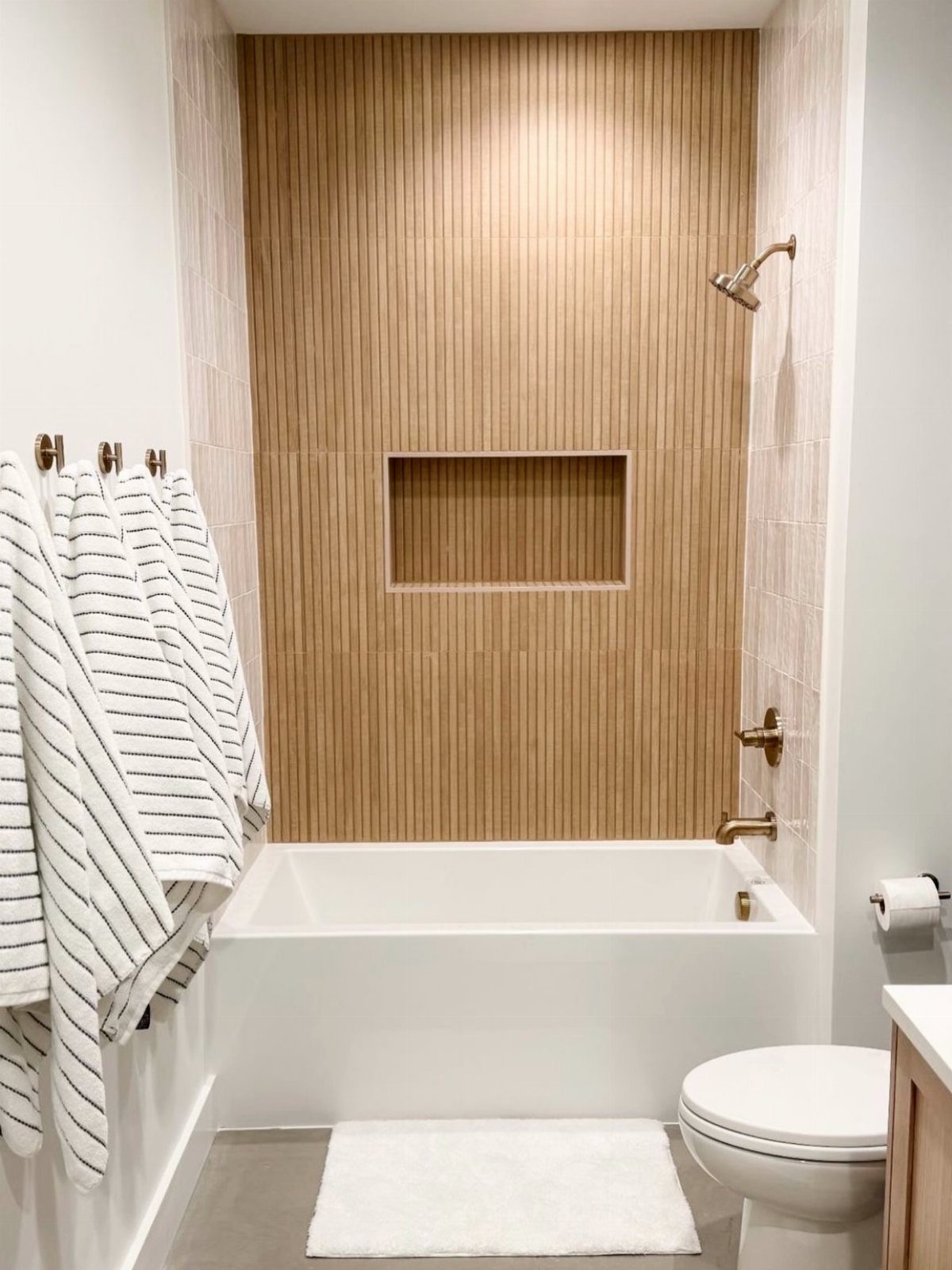 A white bathtub positioned against a vertical wood-look tile accent wall with a built-in niche.