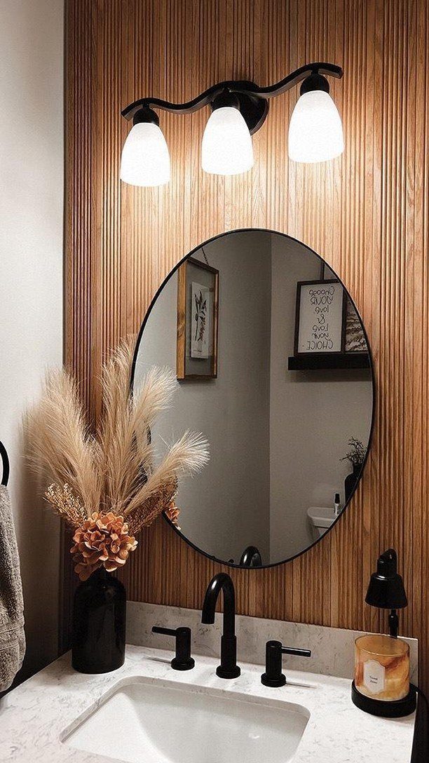 Wood-slat accent wall behind a bathroom vanity with a round mirror and black fixtures.