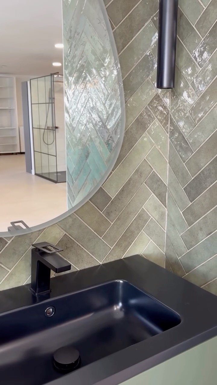 Green and grey Zellige tiles in a herringbone pattern behind a black sink.