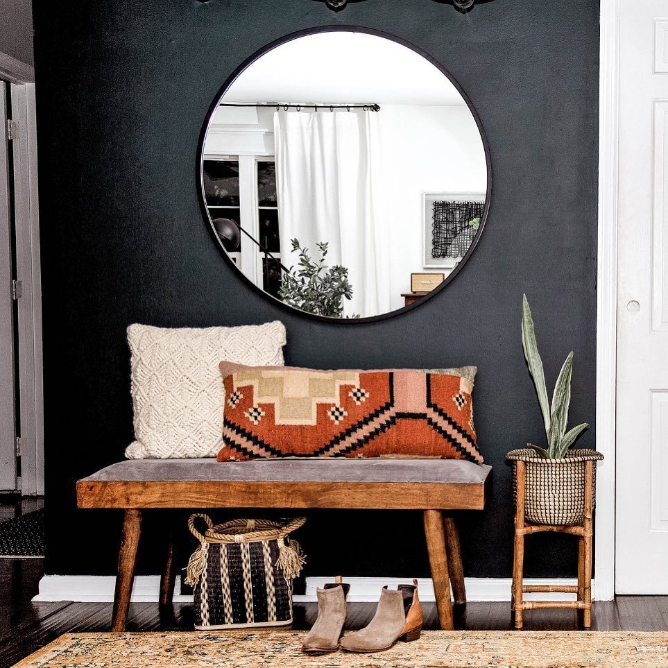 A dark matte black accent wall featuring a round mirror, wooden bench, and decorative pillows.