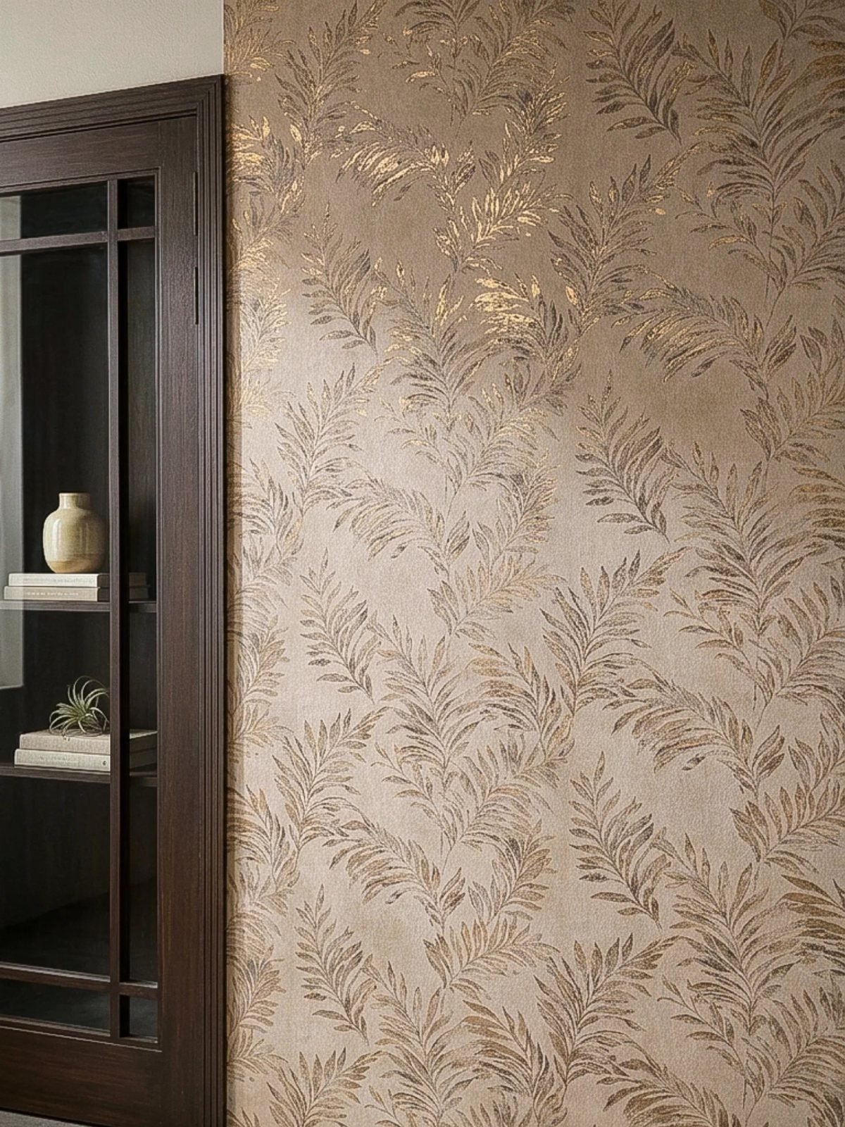 Gold metallic leaf patterns on a textured beige wallpaper accent wall next to a dark wood cabinet.