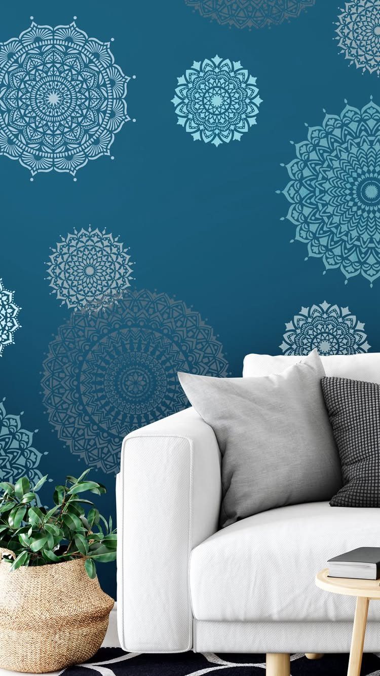 Teal blue wall decorated with large white mandala stencil patterns behind a white sofa.