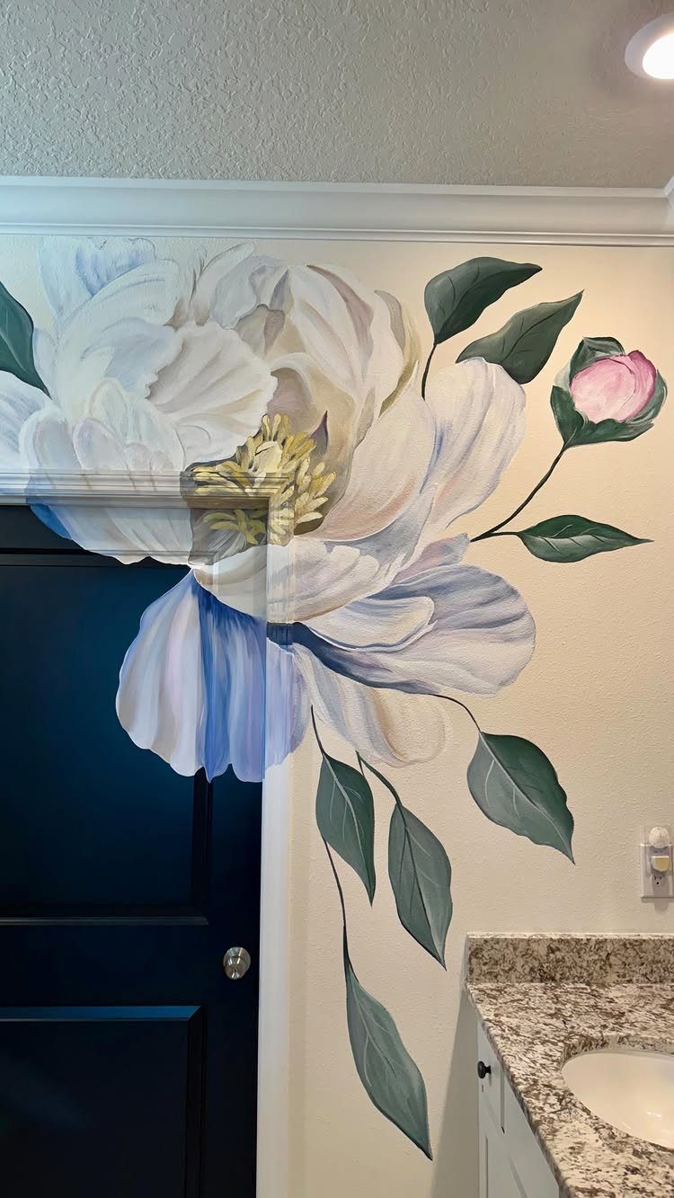 Large hand-painted white peony mural with green leaves on a white wall next to a dark blue door.