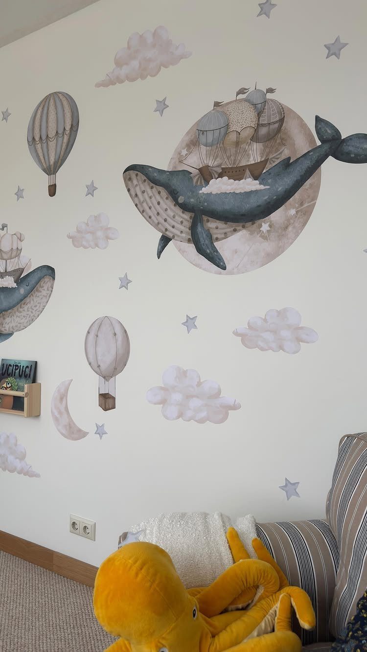 Whale and hot air balloon wall decals decorating a white nursery wall above a sofa.