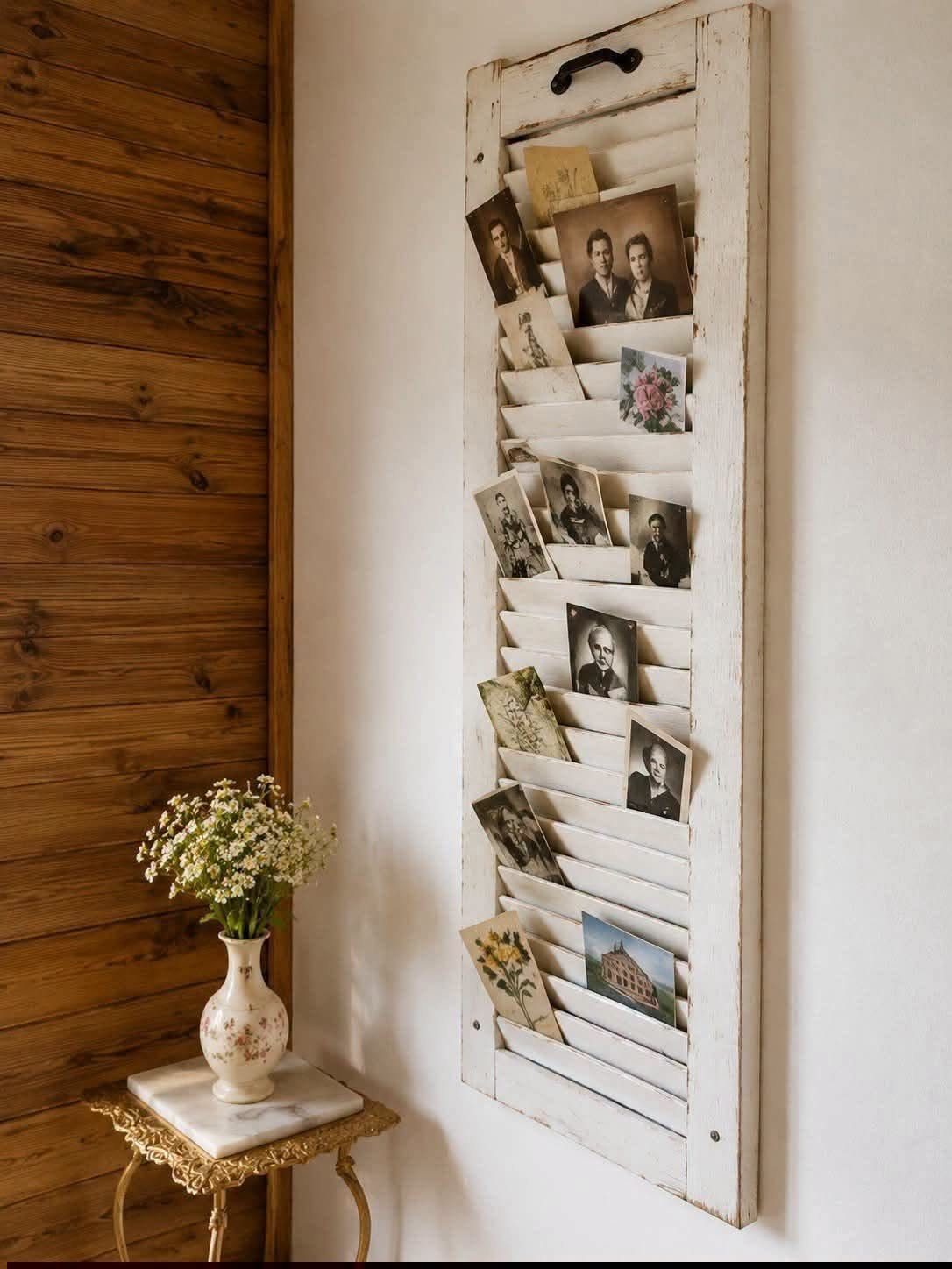 Vintage photographs tucked into the slats of a white weathered wooden shutter mounted on a wall.