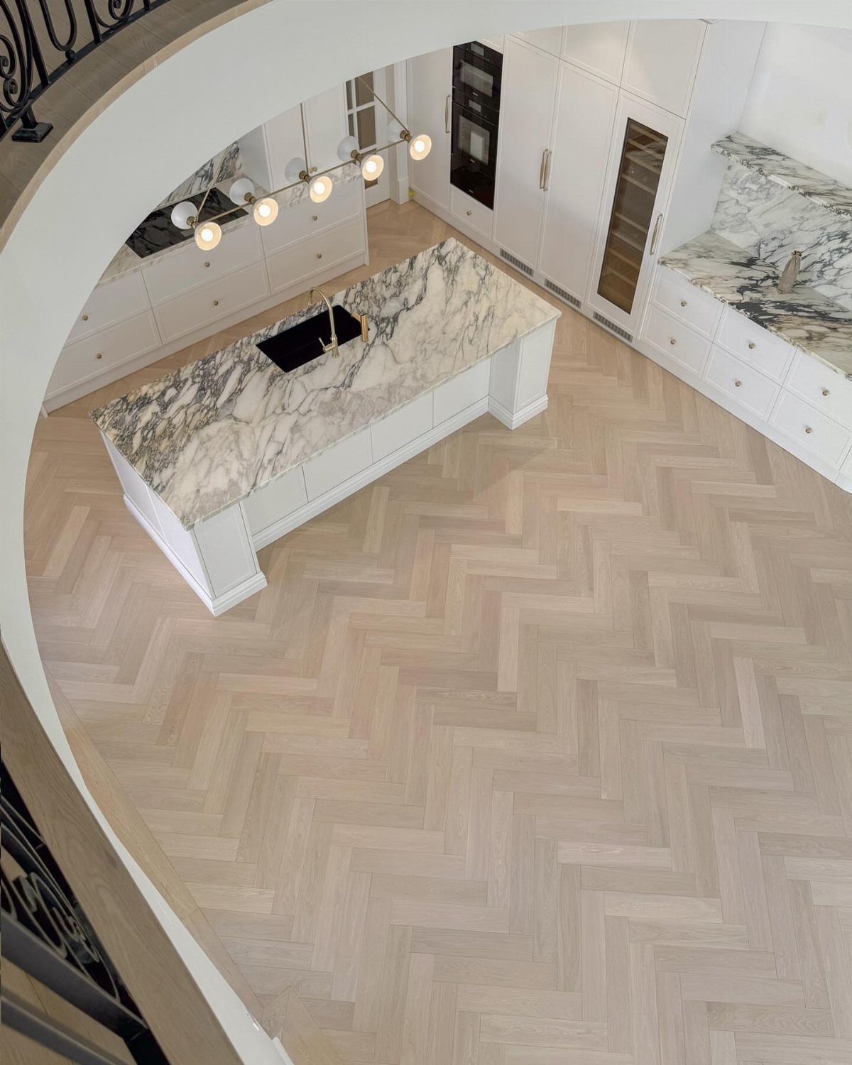 Kitchen Floor Colors: 14 Ideas for 2026 8 Light wood herringbone pattern flooring in a modern white kitchen with a marble island.