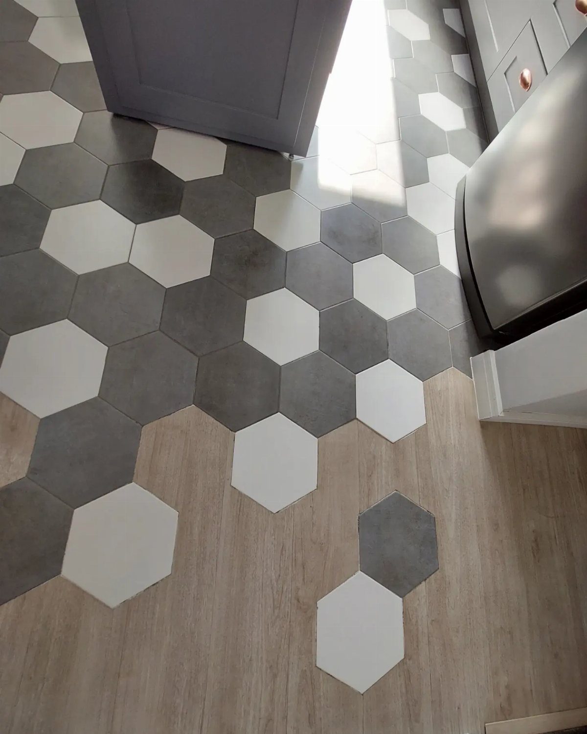Kitchen Floor Colors: 14 Ideas for 2026 4 Hexagon tiles in white and gray transitioning into light wood-look flooring in a kitchen.