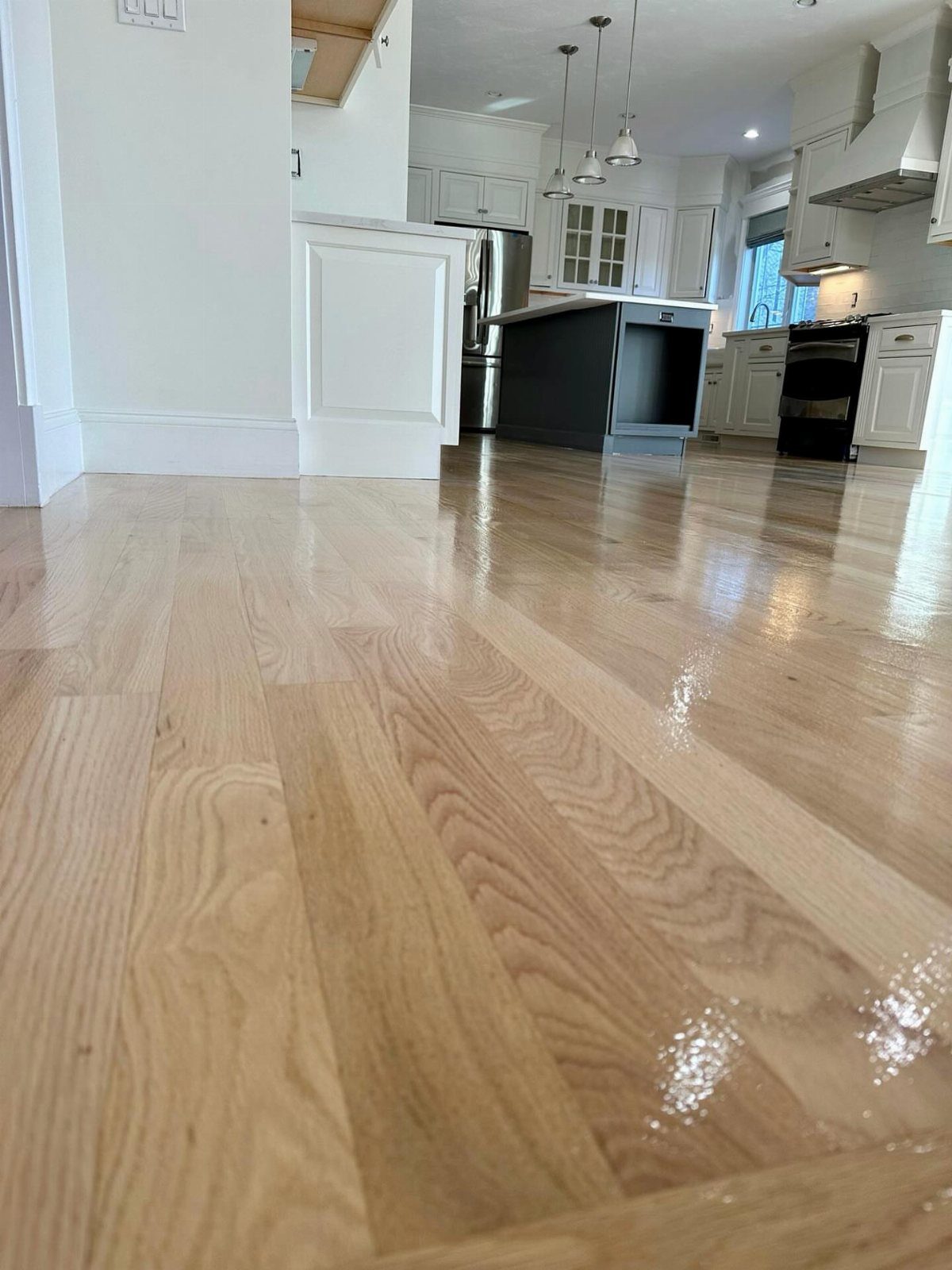 Kitchen Floor Colors: 14 Ideas for 2026 12 Light wood plank flooring with a glossy finish leading into a modern white kitchen.