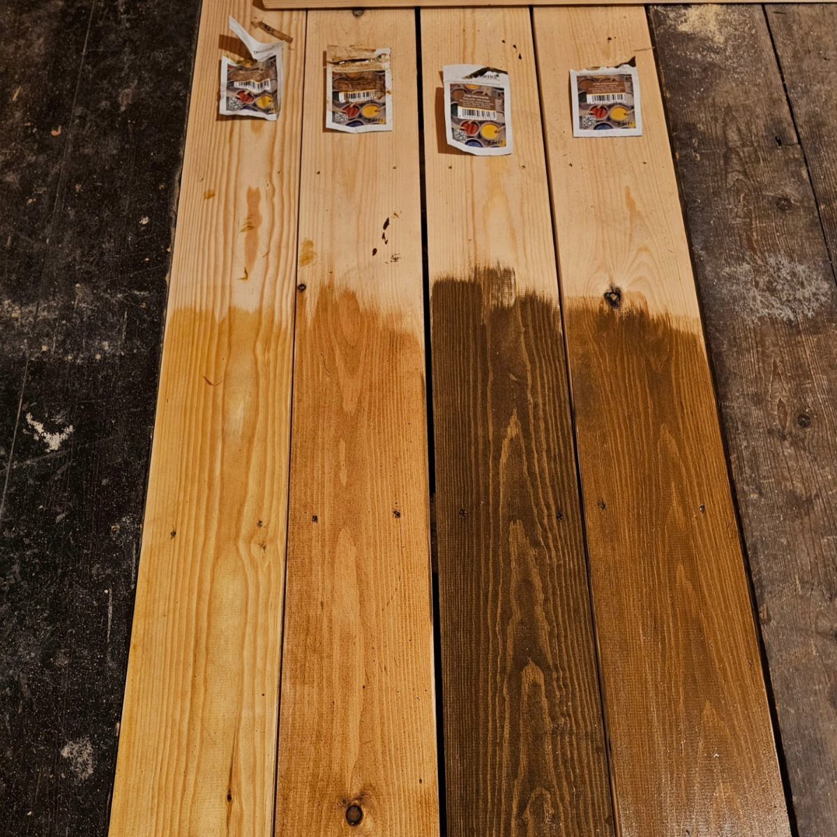 Kitchen Floor Colors: 14 Ideas for 2026 7 Four wooden planks with different brown stain samples laid side by side on a dark floor.
