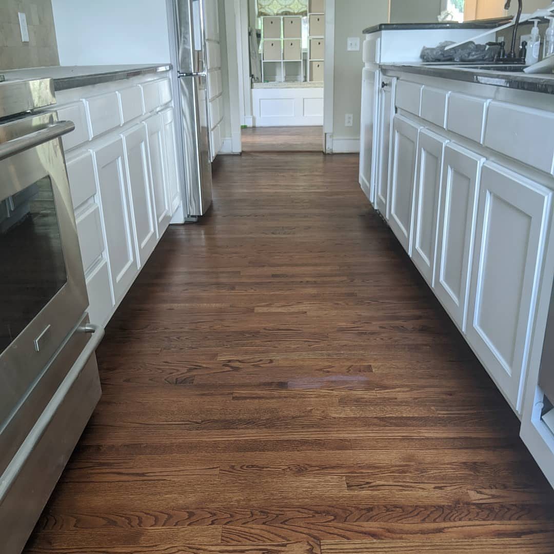 9 Kitchen Hardwood Flooring Ideas for Light to Bold Contrast 2 Medium brown hardwood flooring installed in a kitchen with white cabinets and stainless steel appliances.