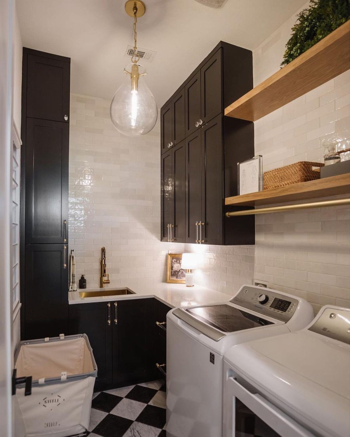 Black and white checkered flooring in a modern laundry room with black cabinets and white appliances.