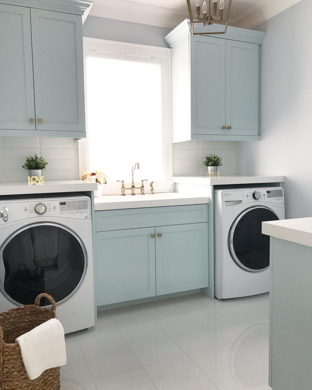 Light blue laundry room cabinets with white appliances and glossy tile flooring.