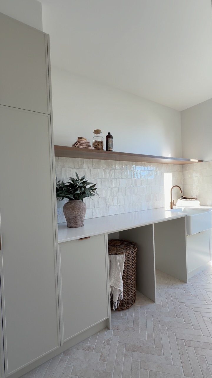 Light grey herringbone tile flooring in a modern, bright laundry room with white cabinetry.