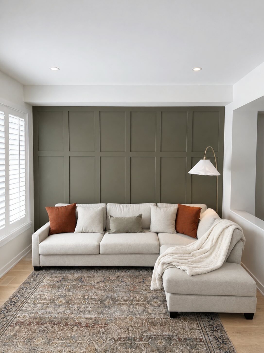 A cream sectional sofa sits against an olive green board and batten accent wall.