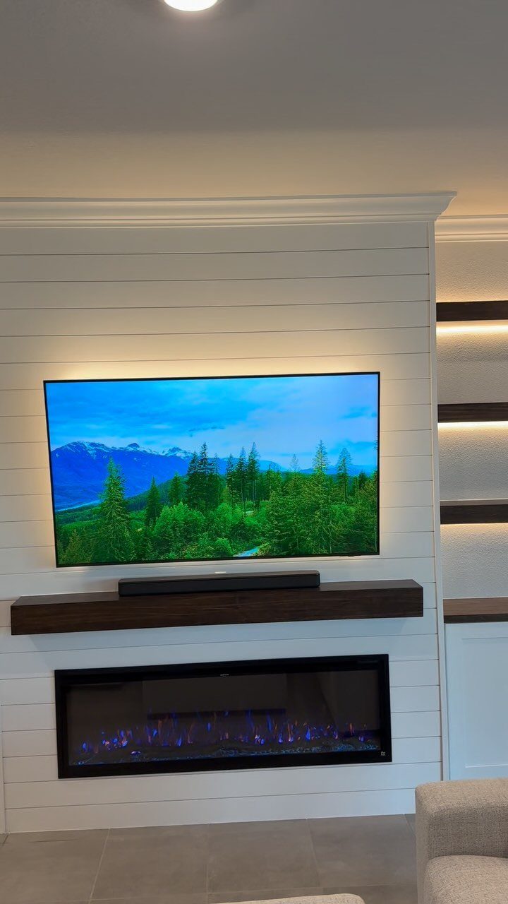 White shiplap accent wall with a television, wooden mantel, and electric fireplace.