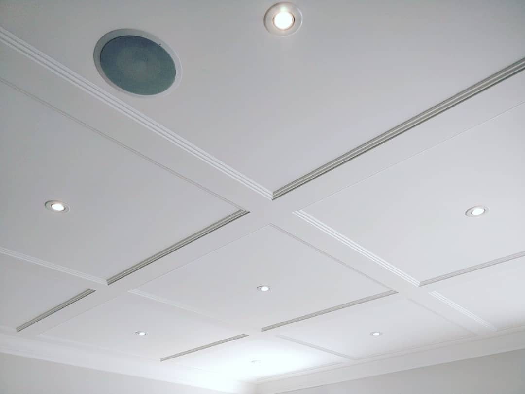 A white waffle ceiling with recessed lighting and a circular vent in a room.