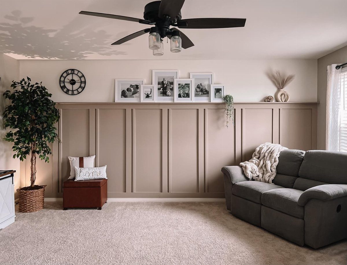Beige wainscoting with vertical panel moulding on a living room wall behind a grey sofa.