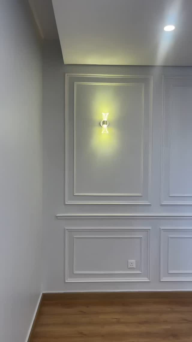 Light grey wall with decorative rectangular molding and a glowing wall sconce.