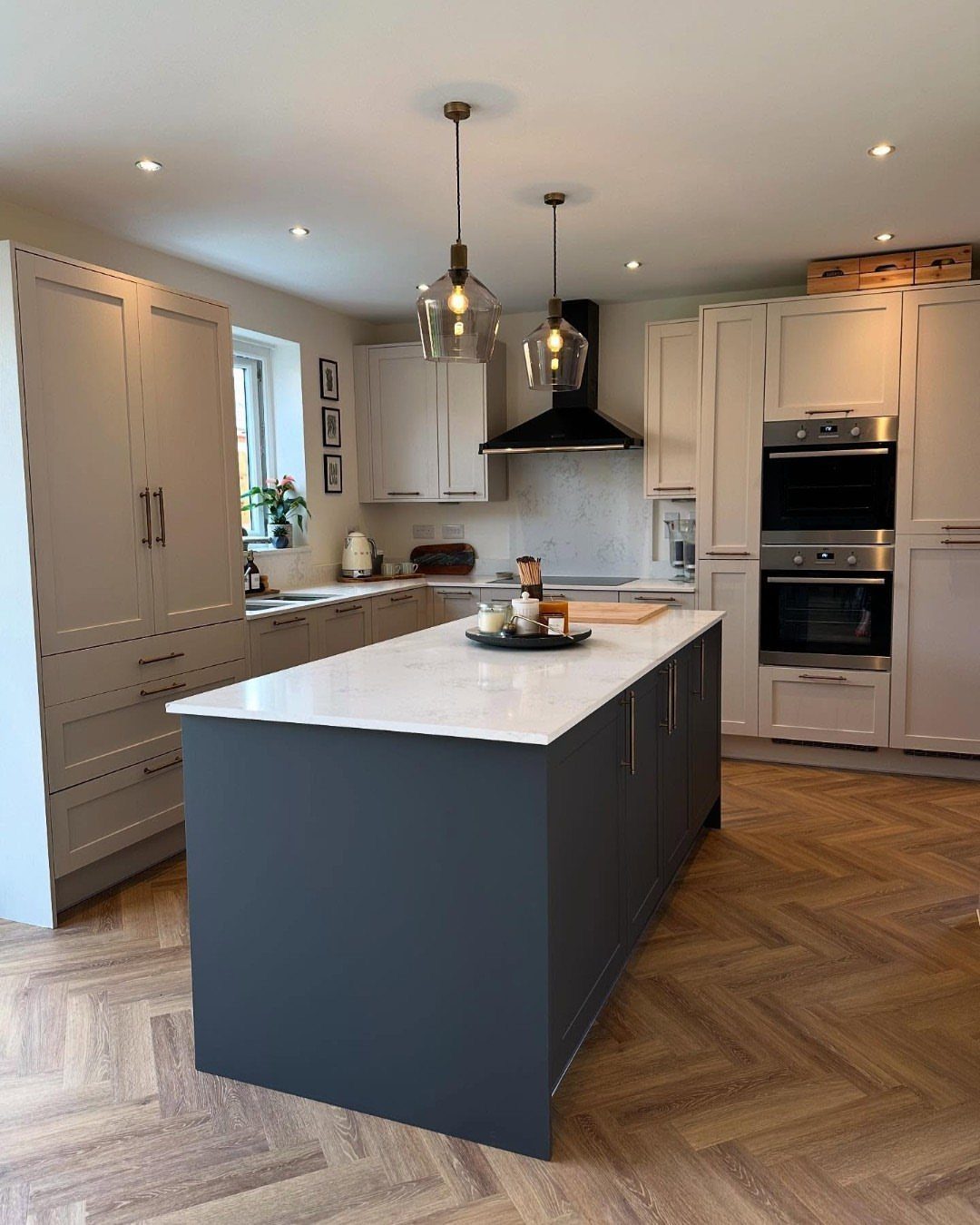 Most Popular Coretec Colors: 8 Best-Selling Flooring Picks 7 A modern kitchen with a dark grey island, white countertops, and light wood herringbone flooring.