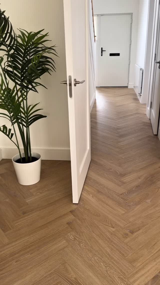 Most Popular Coretec Colors: 8 Best-Selling Flooring Picks 4 Light beige herringbone wood flooring in a bright hallway with a white door and potted plant.