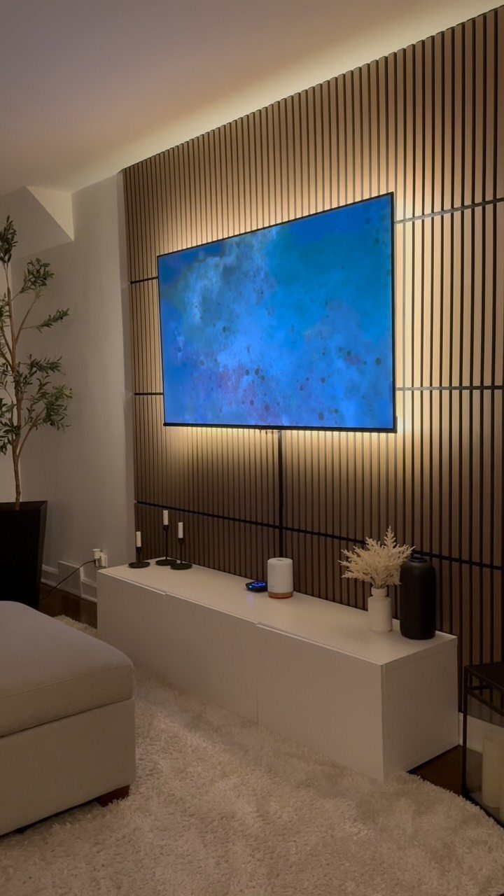 Vertical wooden fluted PVC panels covering a wall behind a large television and white console.