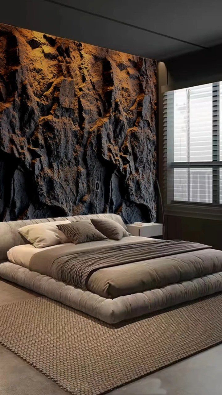 Textured stone look wall panels behind a modern low-profile bed in a dark bedroom.