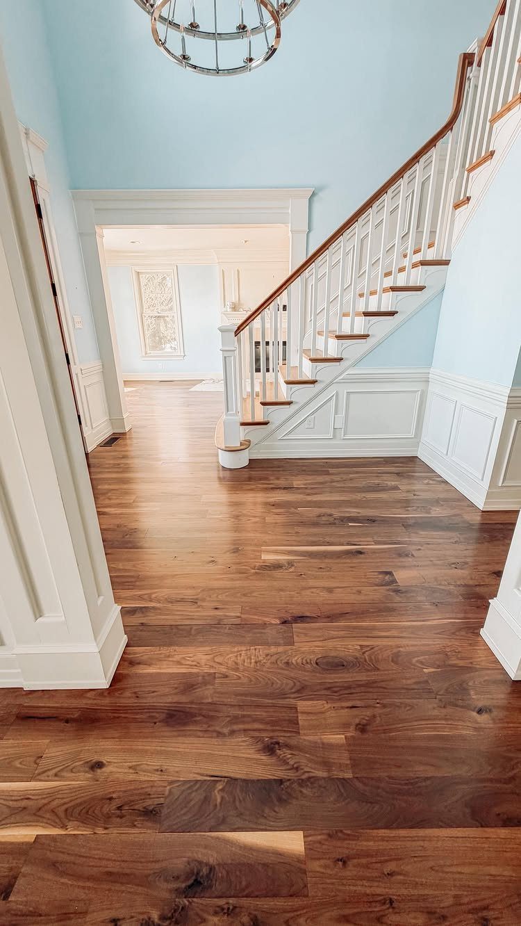 Walnut hardwood flooring with rich brown grain patterns in a bright hallway with white stairs.