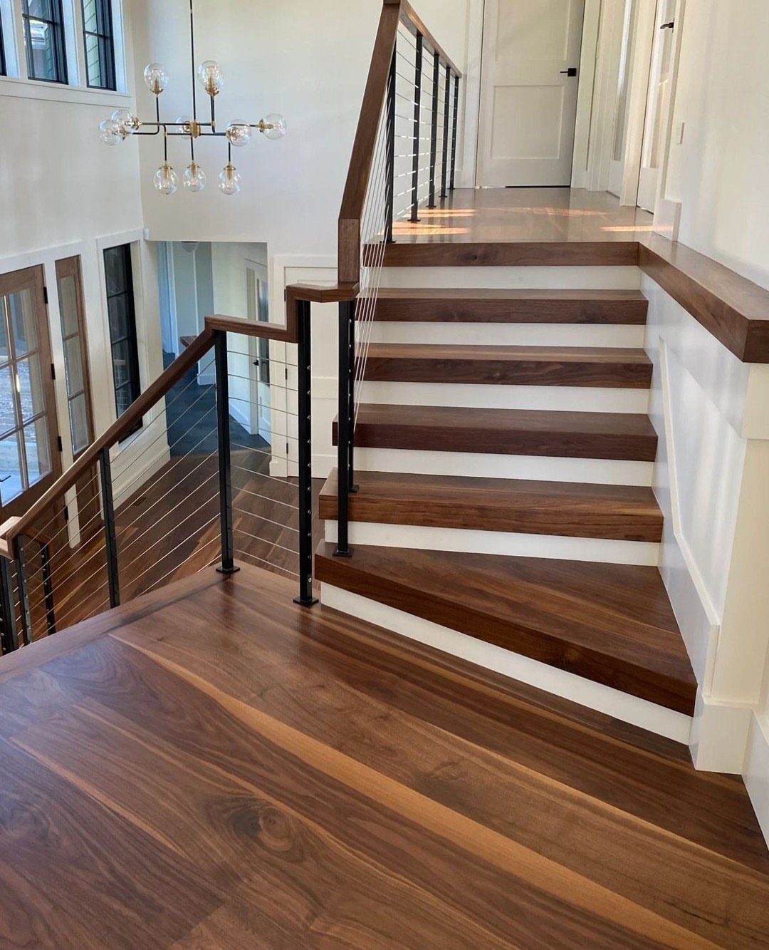 Dark walnut hardwood flooring on a staircase landing and wooden stair treads in a bright home.