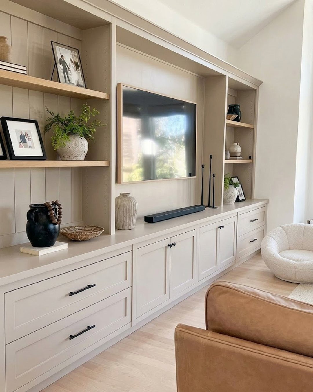 Built-in beige entertainment unit with open shelving, a television, and lower storage cabinets in a modern living room.