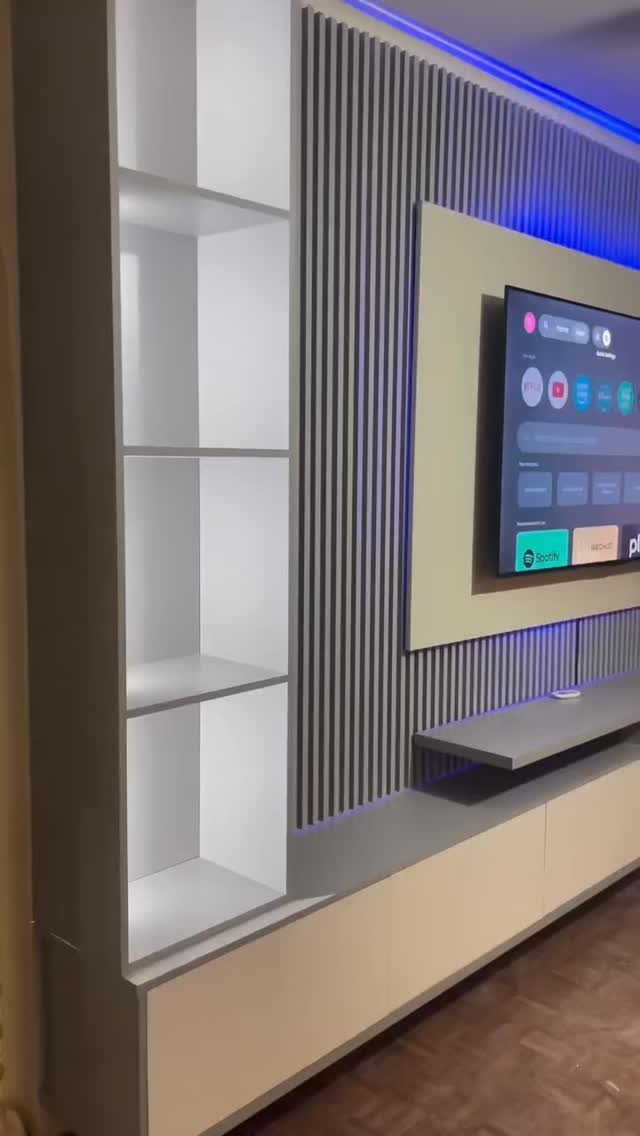 Modern TV wall unit with vertical slats, built-in shelving, and blue LED accent lighting.