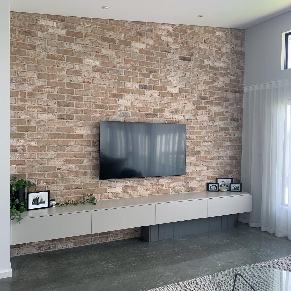 A flat screen television mounted on a light tan exposed brick accent wall above a white console.