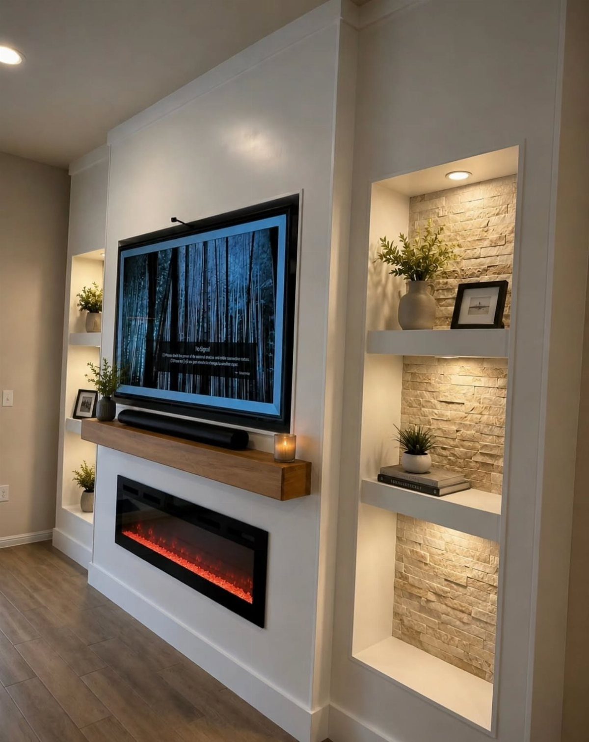 A white built-in wall with a television, wooden mantel, electric fireplace, and recessed stone shelves.